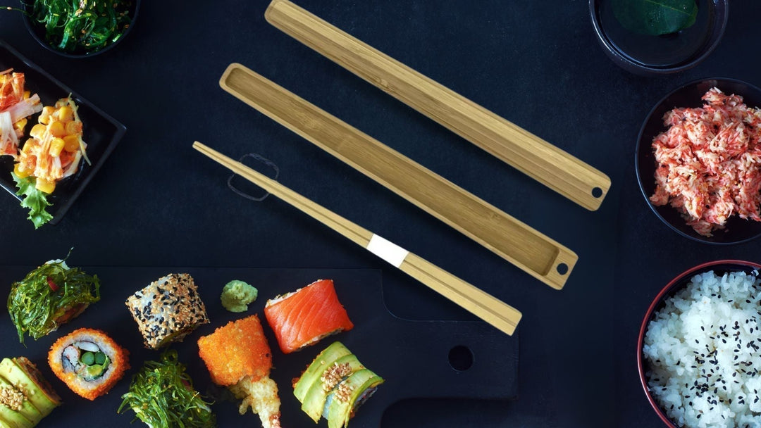 Top-down view of natural bamboo portable chopsticks with cases, set against a dark table with bowls of sushi, rice, and seaweed.