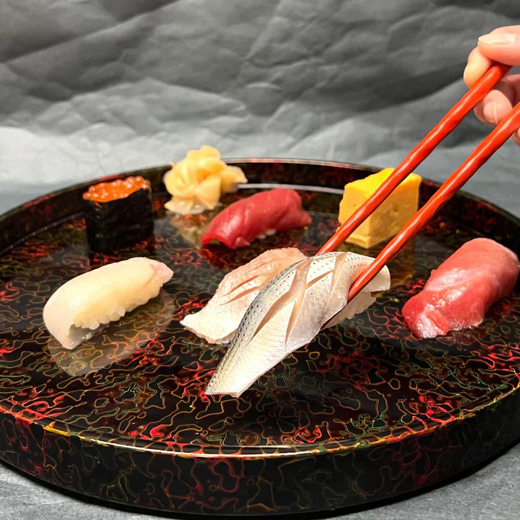A hand using chopsticks to pick up sushi from a decorative plate.
