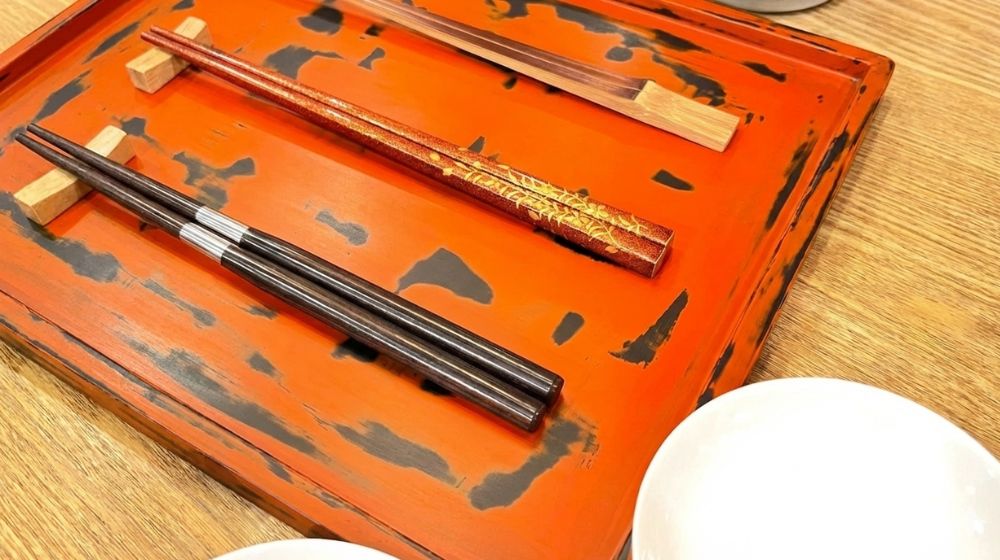Japanese lacquer chopsticks with gold design on red tray.