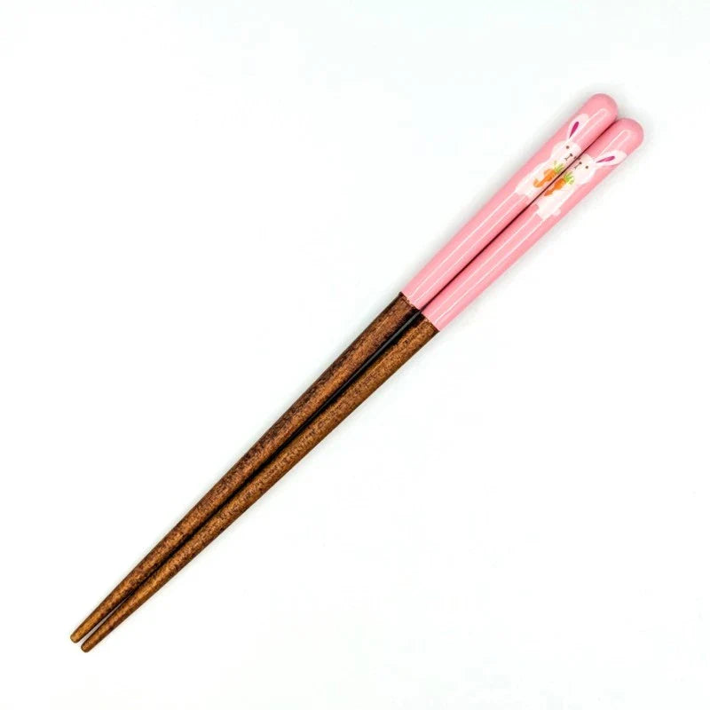 A close-up of a short pair of kids' chopsticks with a pink design featuring a white rabbit holding a carrot.