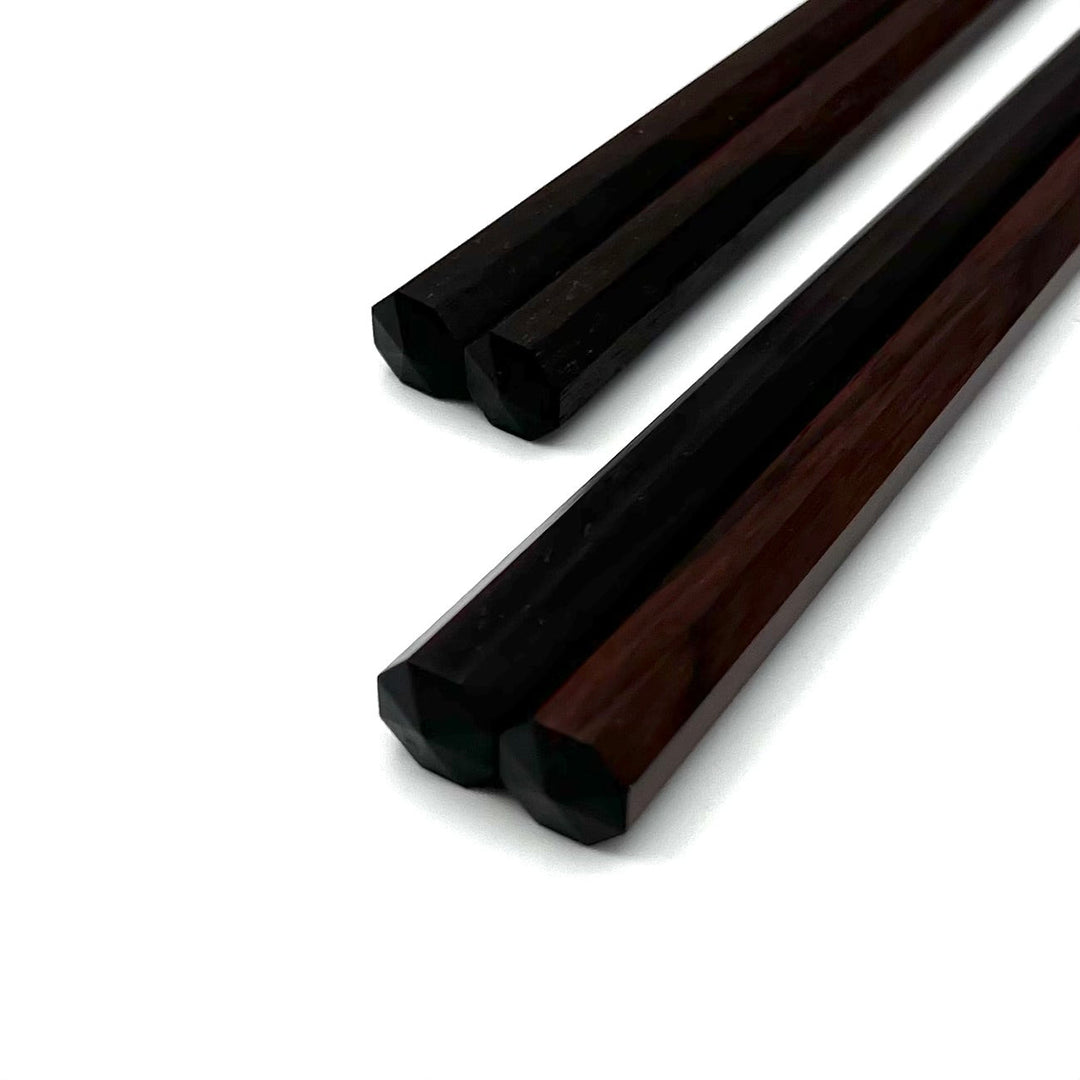 A close-up of the octagonal ends of a pair of ebony chopsticks.