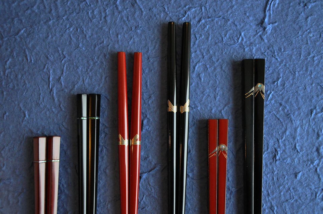 A set of elegant Japanese chopsticks with gold accents, in red, black, and burgundy, arranged on a textured blue background. 